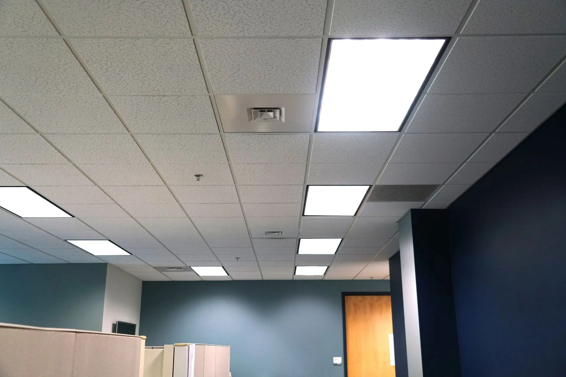 Empty office ceiling with fluorescent lights, teal walls, cubicles, and a wooden door.