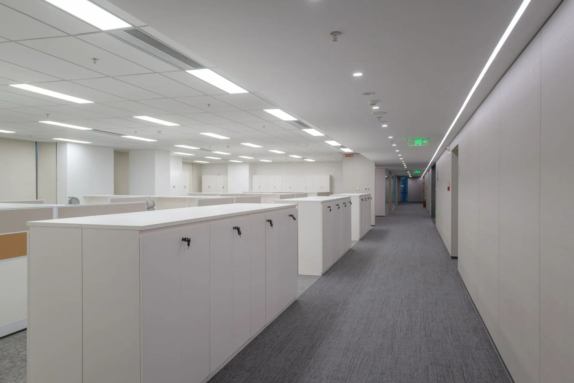 Empty office corridor with white cubicles and gray carpet under bright ceiling lights
