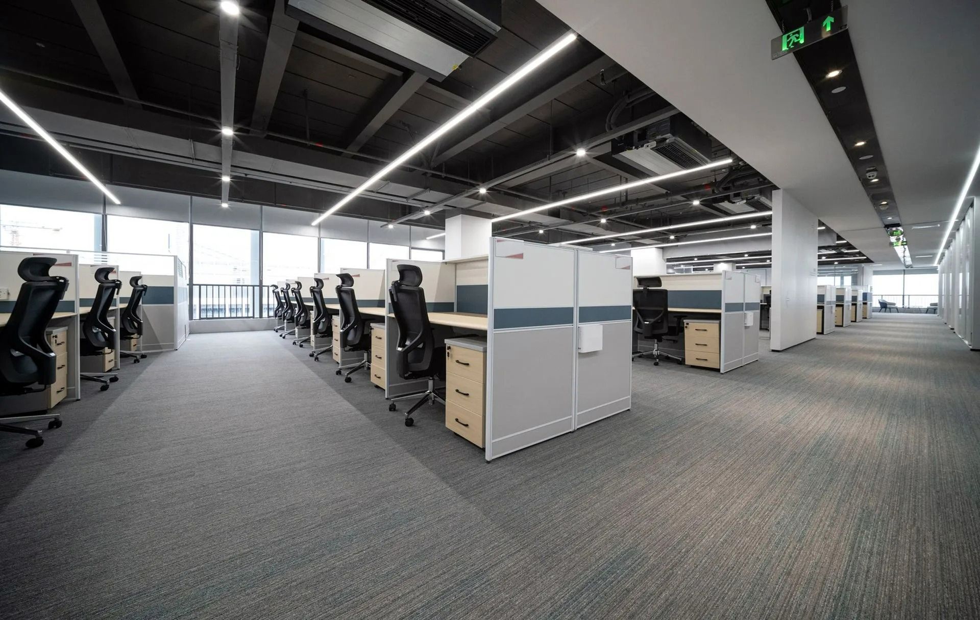 Modern open-plan office with rows of cubicles, desks, and computers under bright ceiling lights