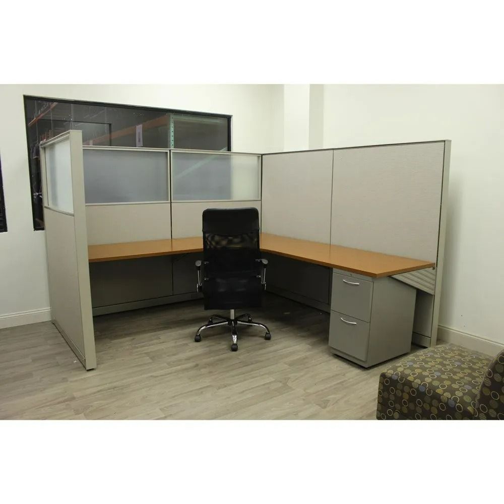 Empty office cubicle with gray partitions, wood desk, black chair, and filing cabinet