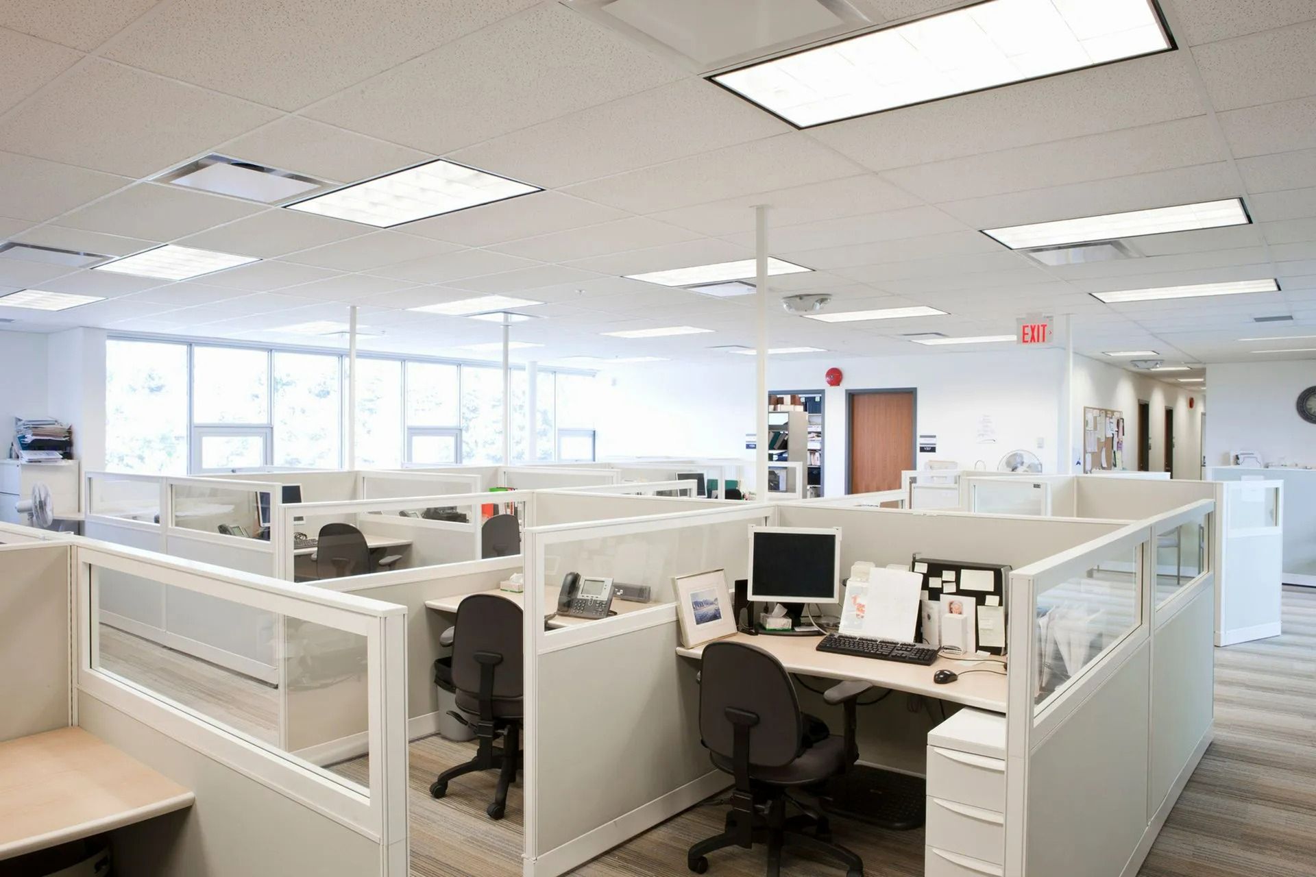 Empty modern office cubicles with desks, computers, and bright overhead lighting