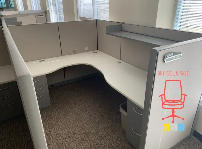 Empty gray office cubicle with white L-shaped desk and chair diagram on the partition