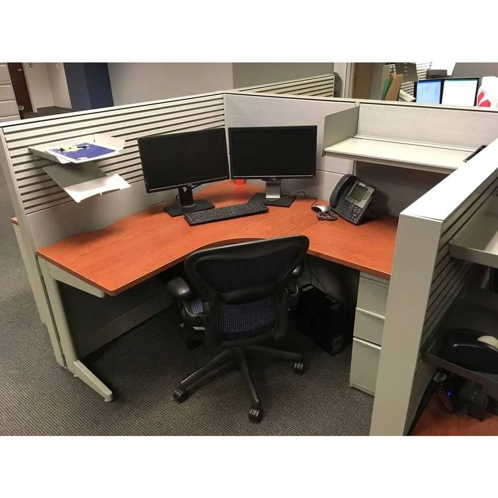 Empty office cubicle with dual monitors, phone, and black chair on a gray carpet.