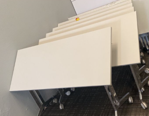 Stacked blank white folding tables on metal carts in an office or storage area.