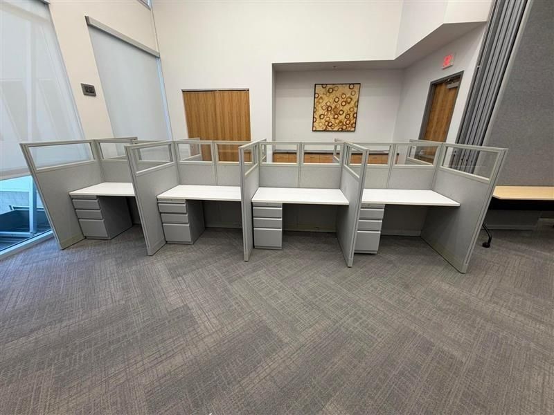 Office lobby with gray carpet, white cubicles, glass railing, and framed wall art