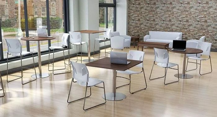 Modern lounge with white chairs, dark tables, and sofas by large windows in a bright, sunlit room
