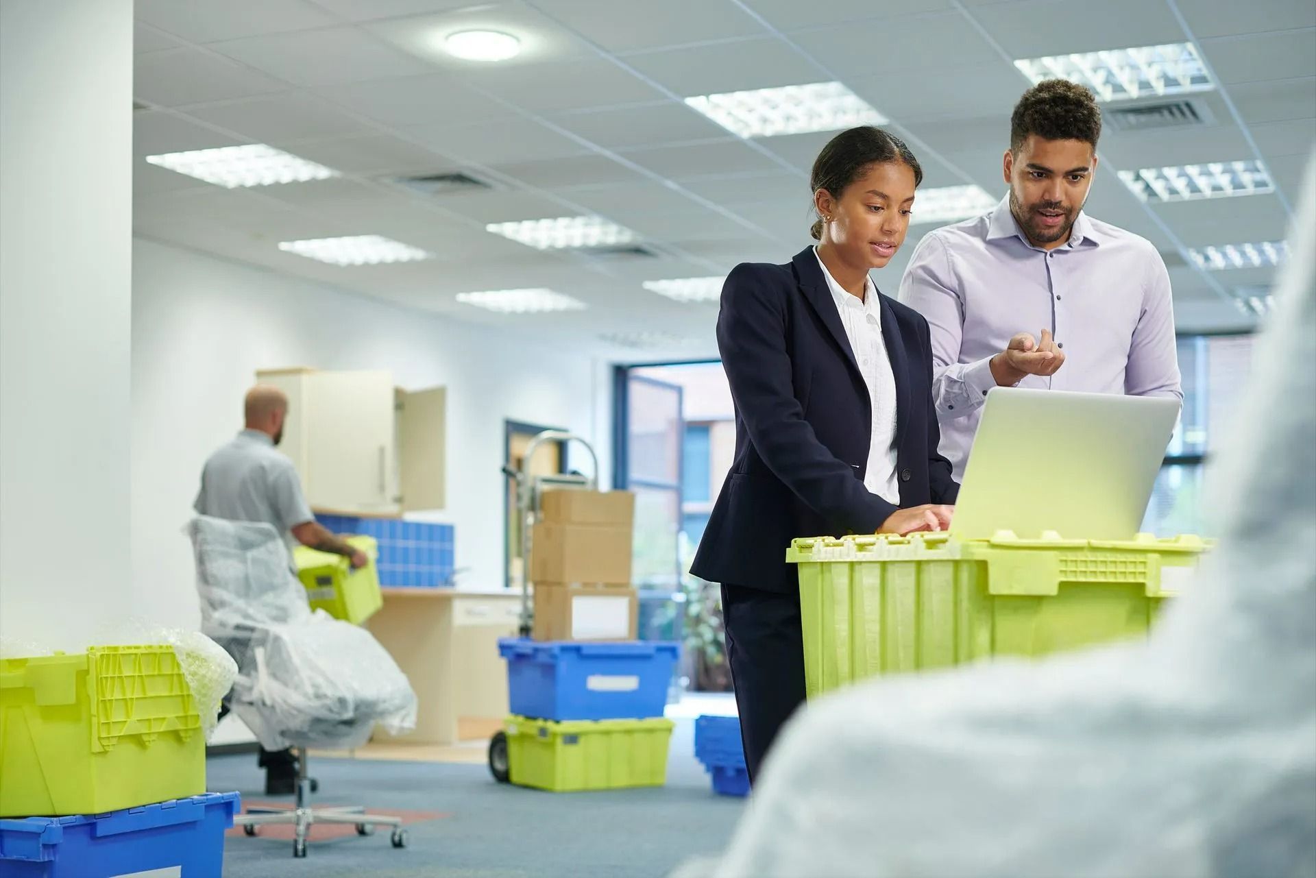 Two coworkers reviewing a laptop in a bright office with colorful storage bins and equipment nearby