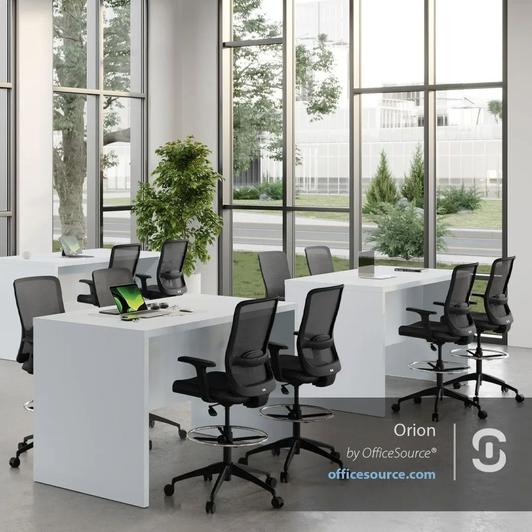 Modern office with white desks, black chairs, and large windows overlooking greenery