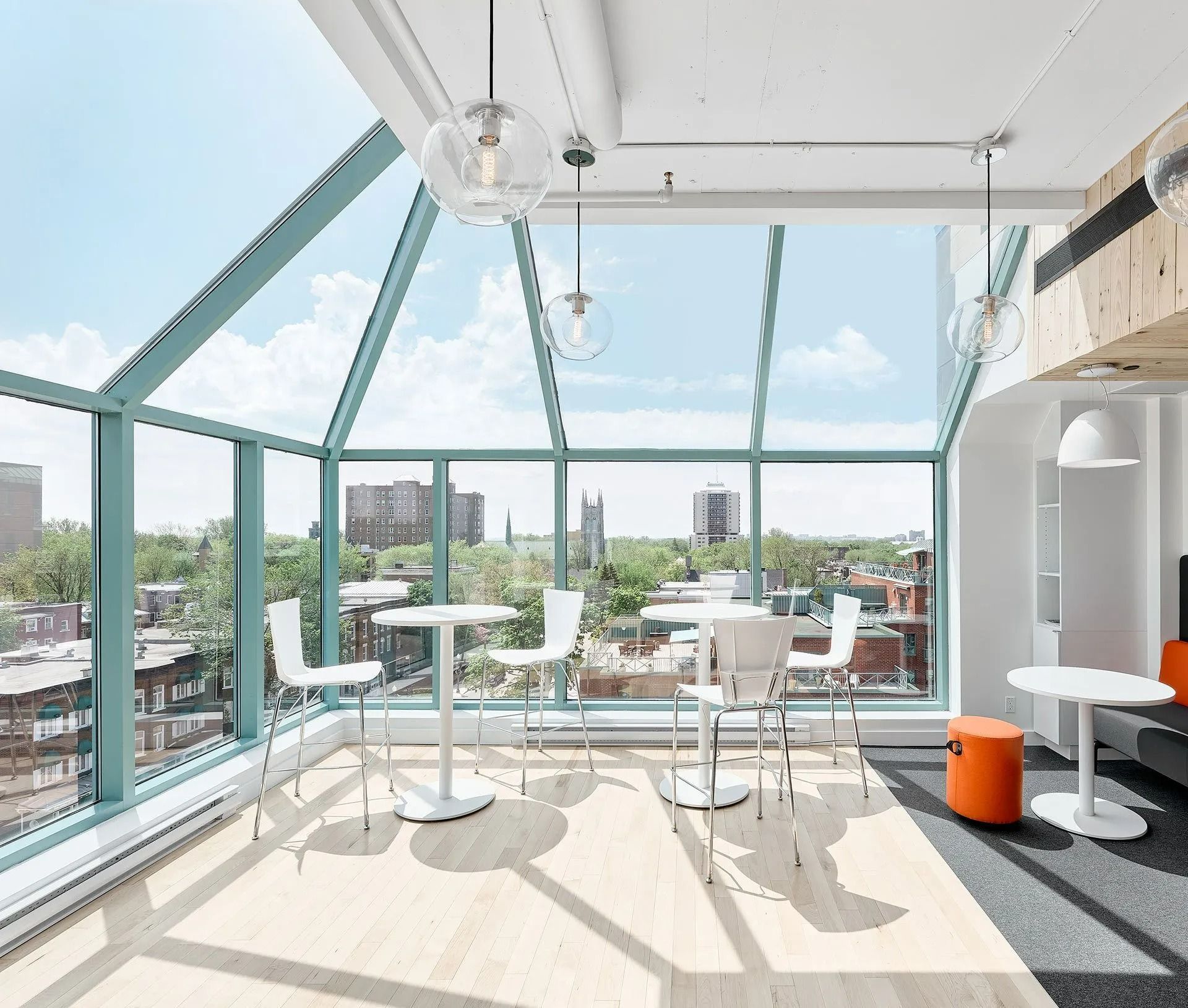 Bright glass-walled café with white tables and stools overlooking a city skyline