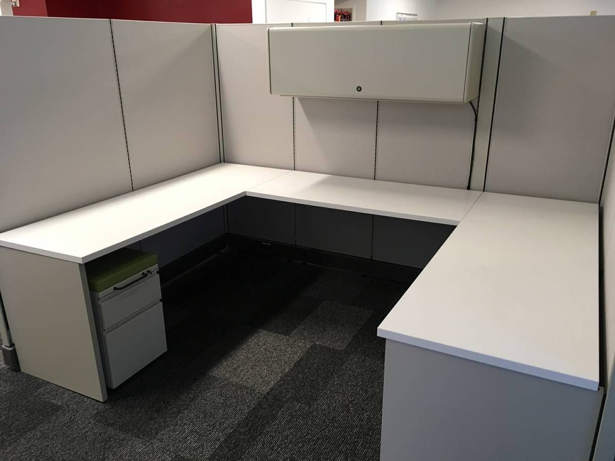 Empty office cubicle with white desks, gray walls, and a black carpeted floor