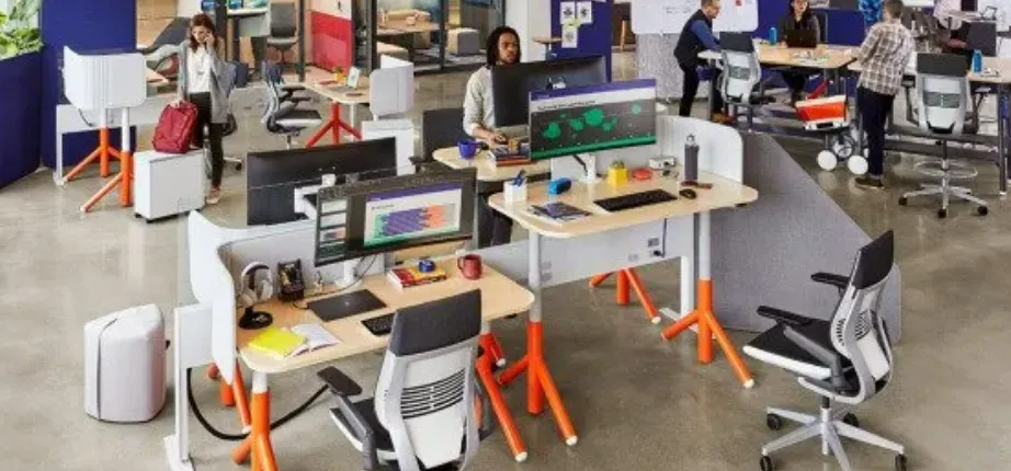 Open-plan office with employees working at desks and computers, bright orange chair legs and dividers