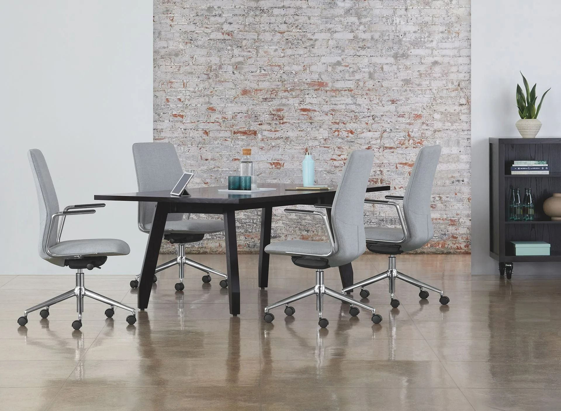 Modern office meeting room with round table, gray chairs, wall art, and a plant on a small cabinet
