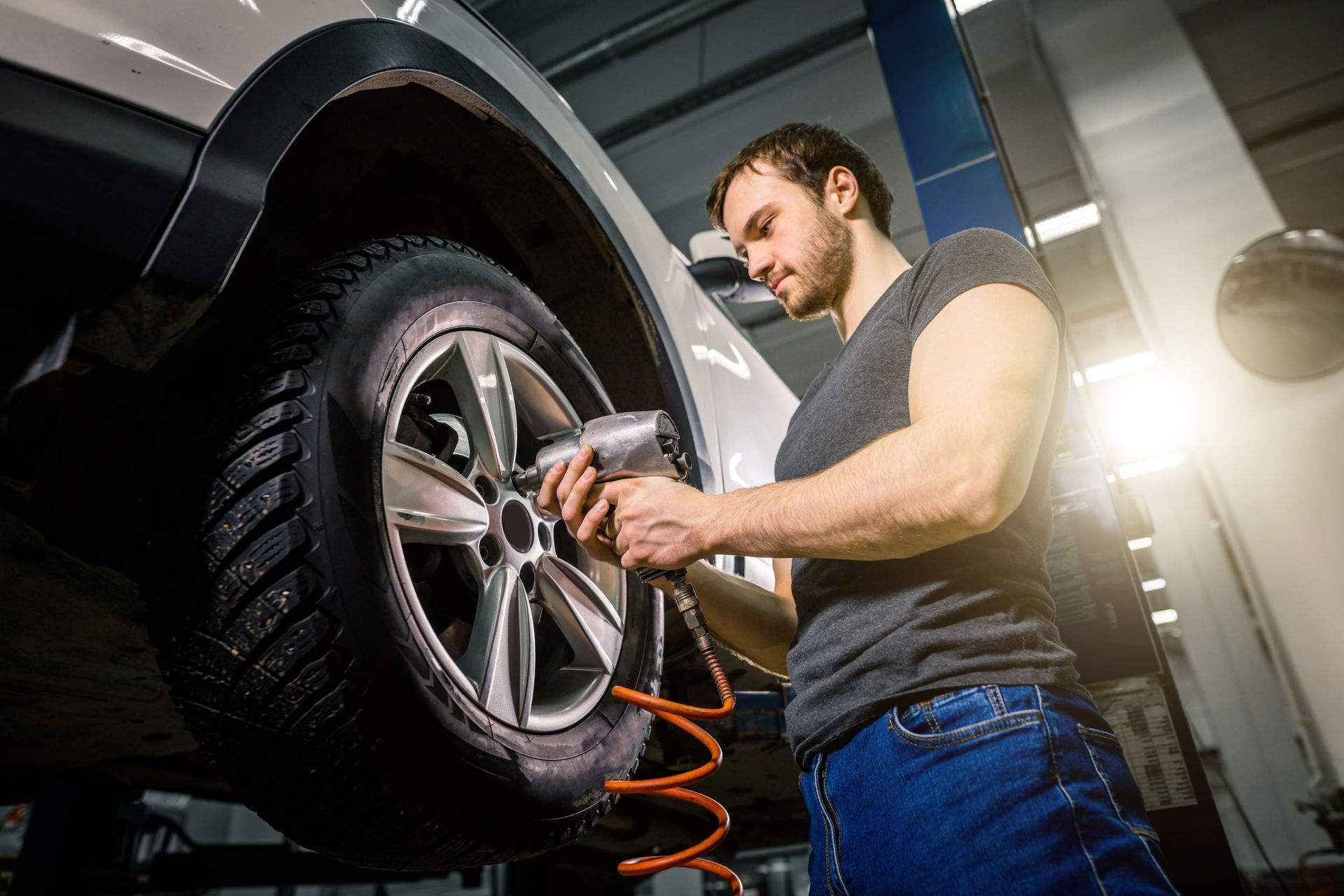 Mechanic using a pneumatic wrench to remove a car's wheel in a garage.