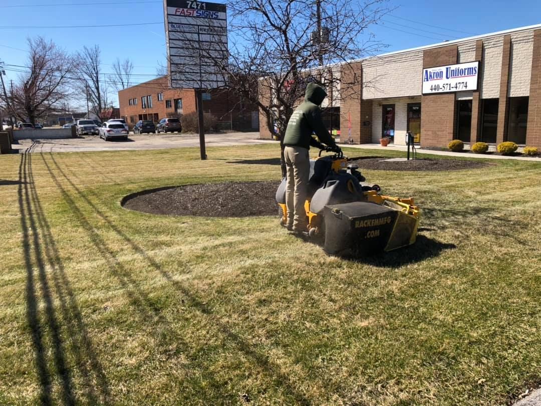 A man is using a lawn mower to cut the grass in front of a building.