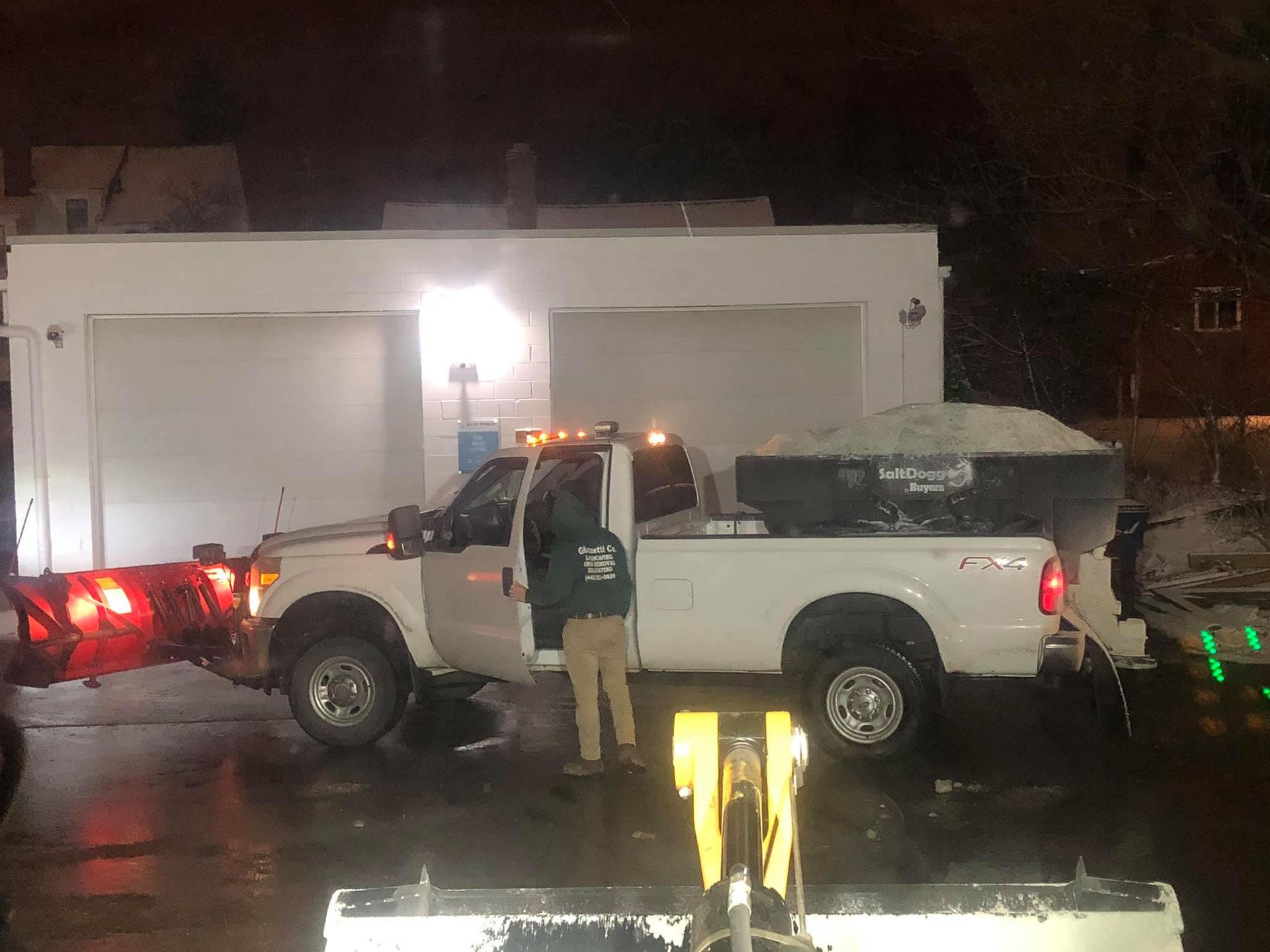A man is standing next to a white truck with a snow plow attached to it.