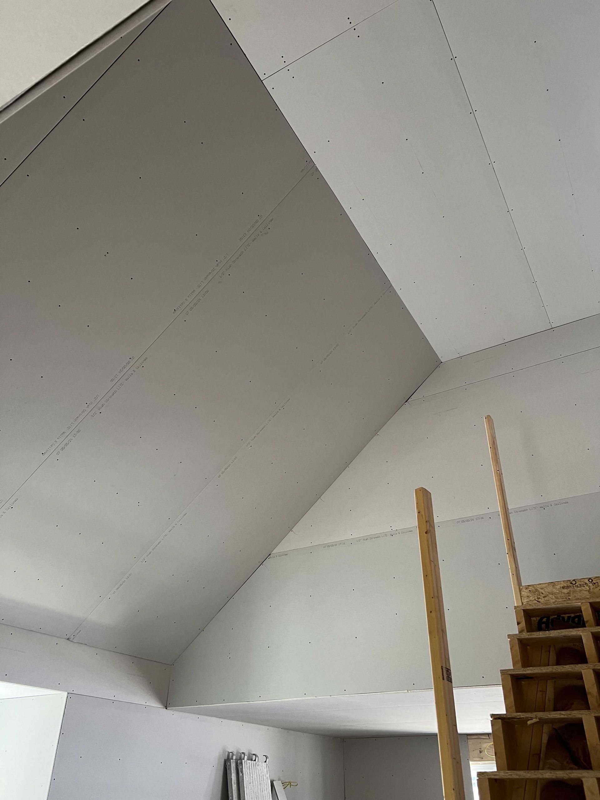 Interior view of a room with unfinished drywall on a sloped ceiling and part of a wooden staircase.