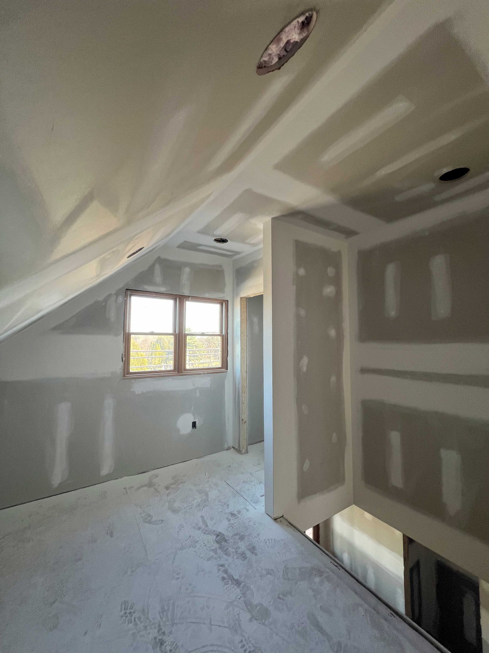 Interior view of a room under construction with drywall on walls and ceiling, a window, and exposed framing.