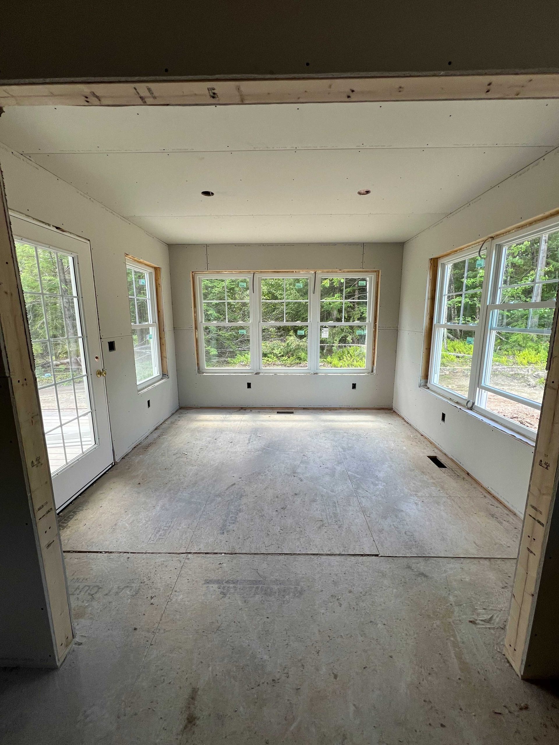 Unfinished room with windows and door. Drywall walls, concrete floor, wooden frames.