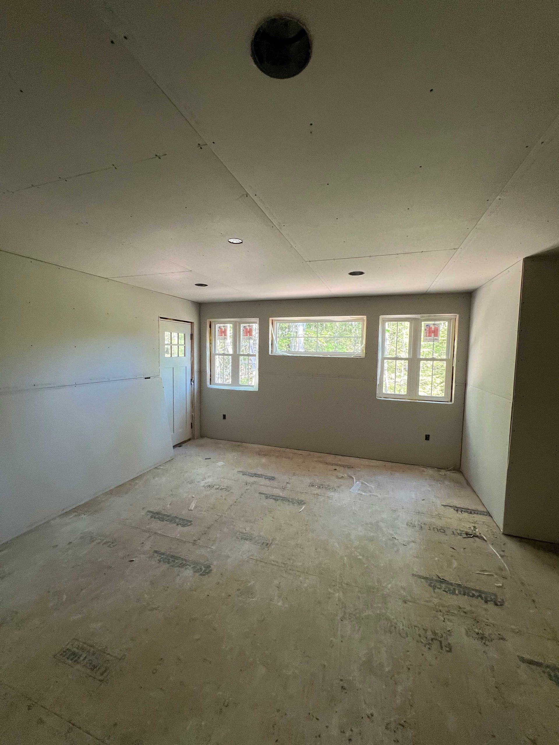 Unfinished interior room with drywall, windows, door, and a textured floor.