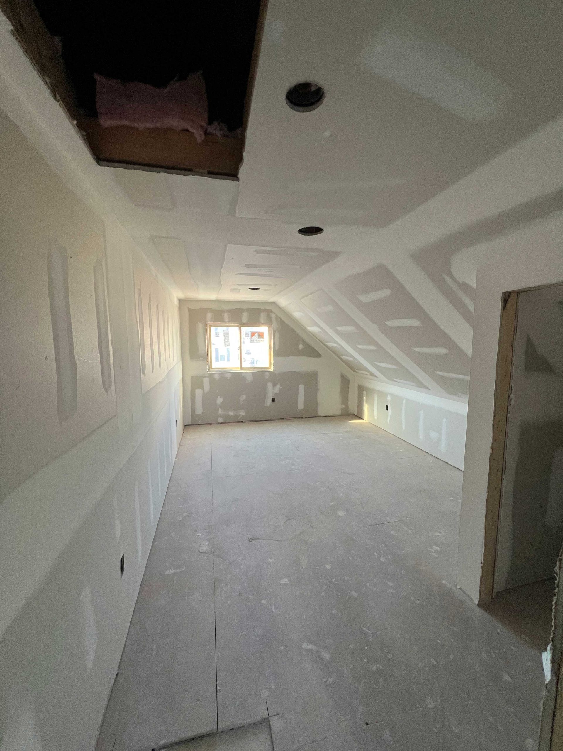Interior of a room under construction with drywall on walls and sloped ceiling; unfinished flooring.