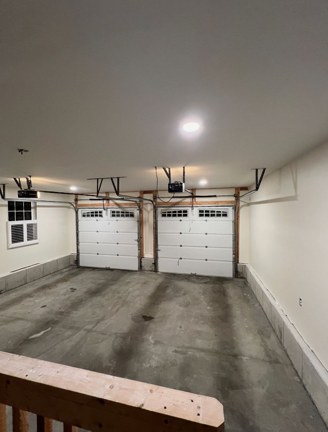Two-car garage interior with white garage doors and a concrete floor.