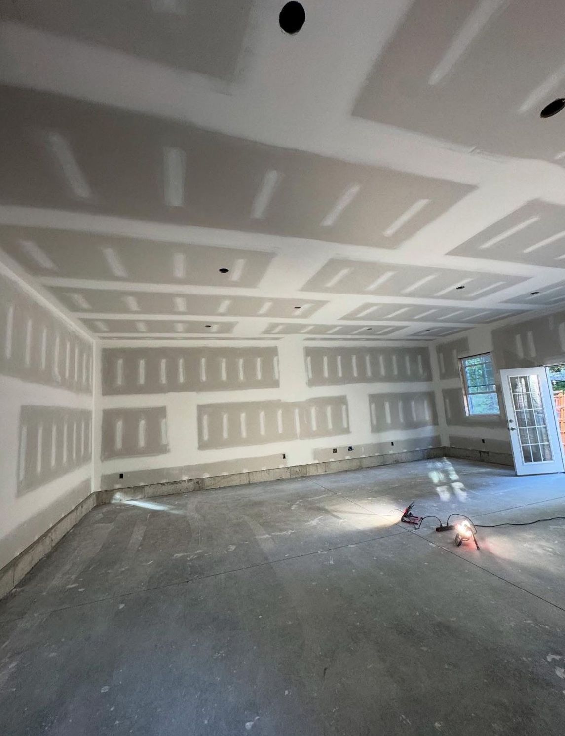 Interior of a room under construction with drywall installed on walls and ceiling, concrete floor.