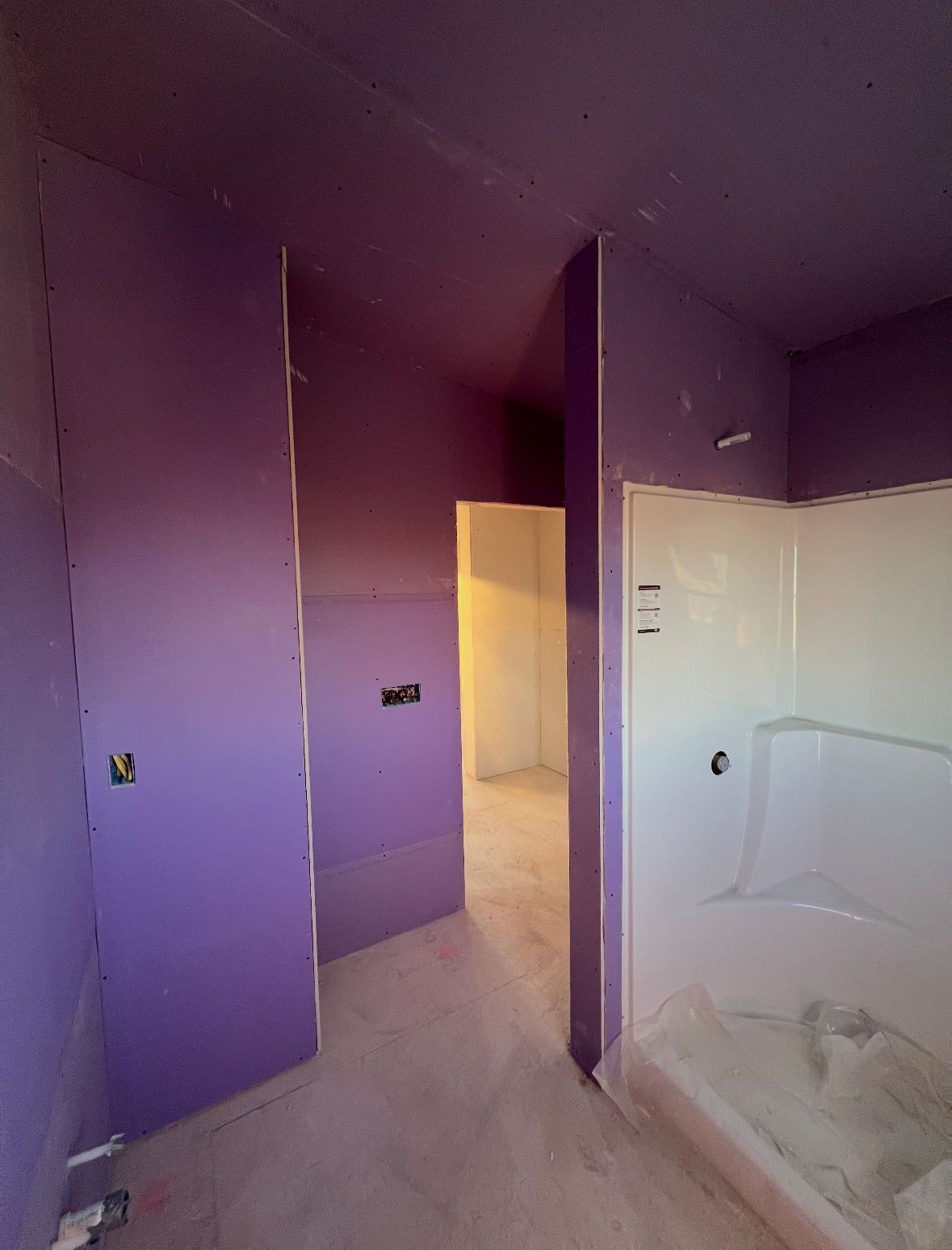 Interior of a room under construction, with purple walls and a white shower stall. A doorway leads to another room.