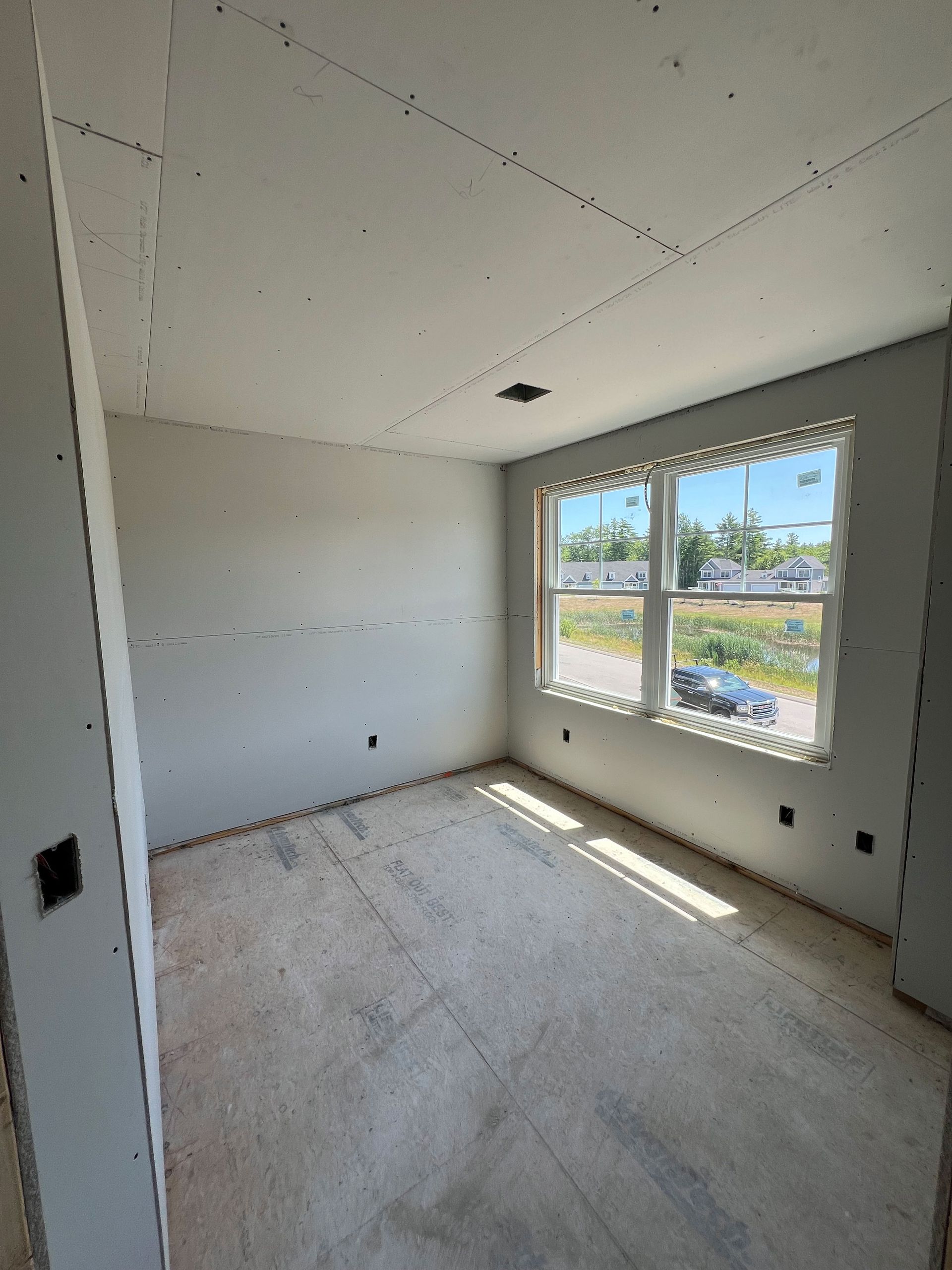 Unfinished room with drywall walls and window. Sunlight streams in. Electrical outlets visible.