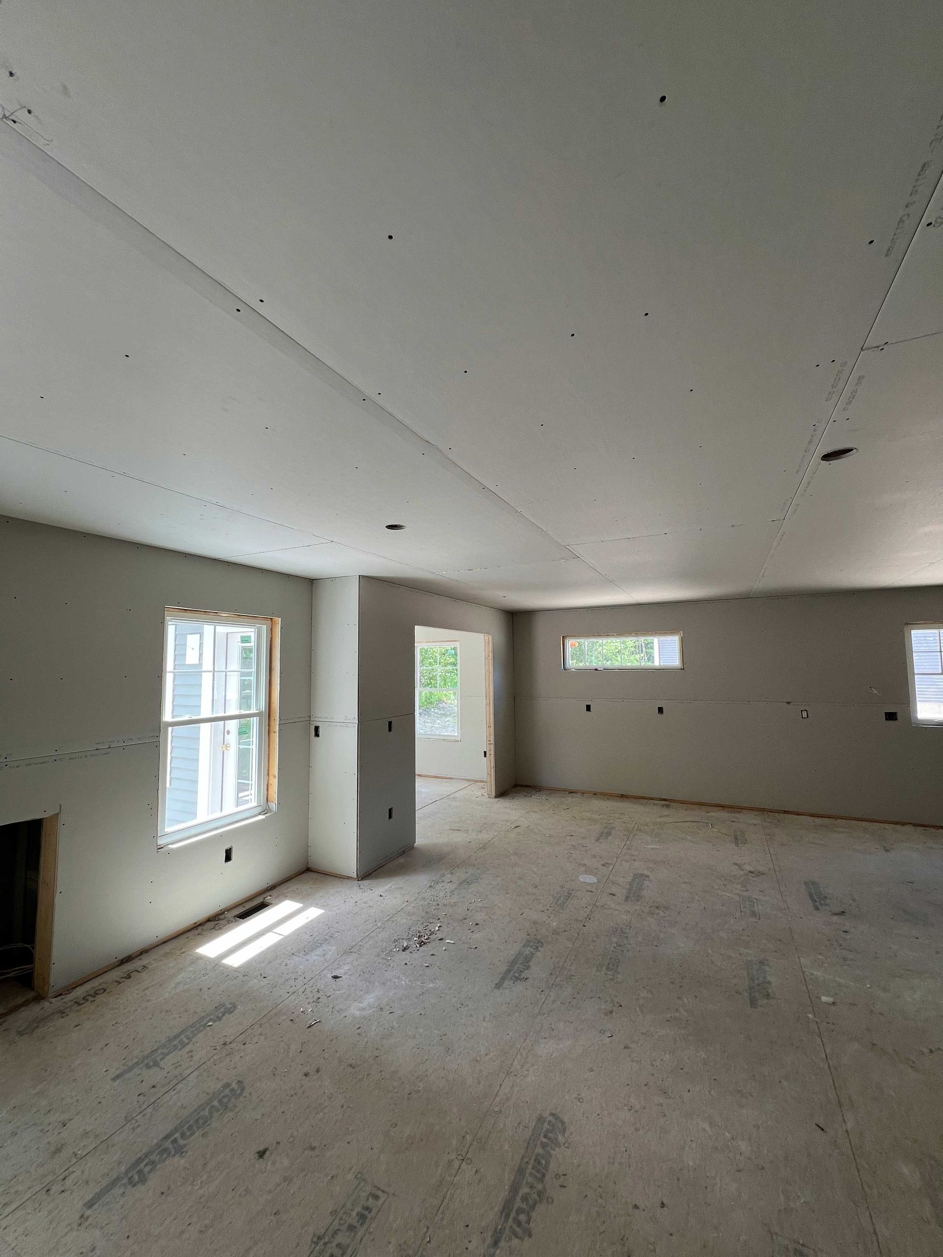 Interior of a room under construction, with drywall walls and ceiling, windows, and a doorway.