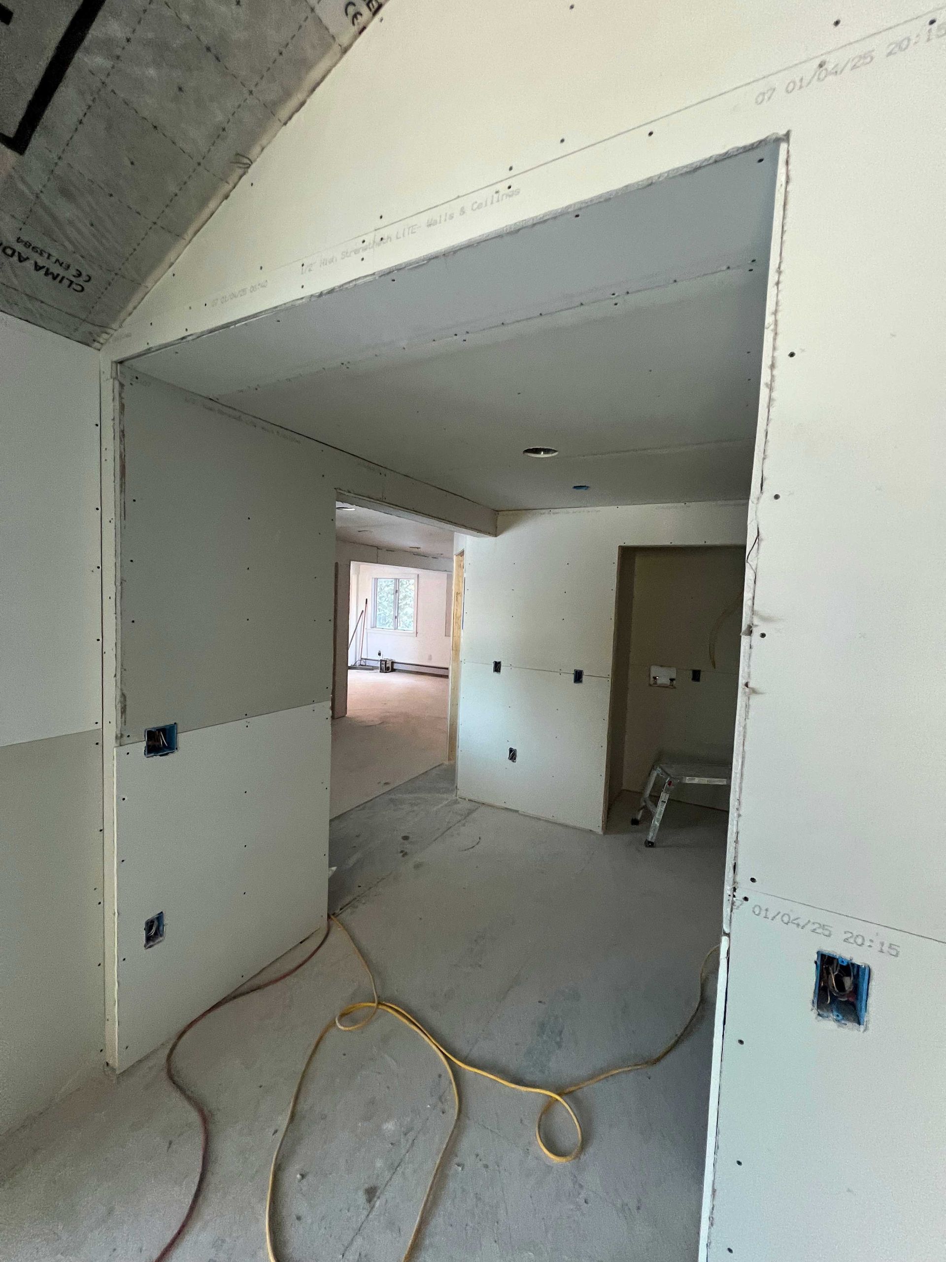 Interior doorway in a building under construction, showing drywall and electrical boxes. A yellow cord lies on the floor.