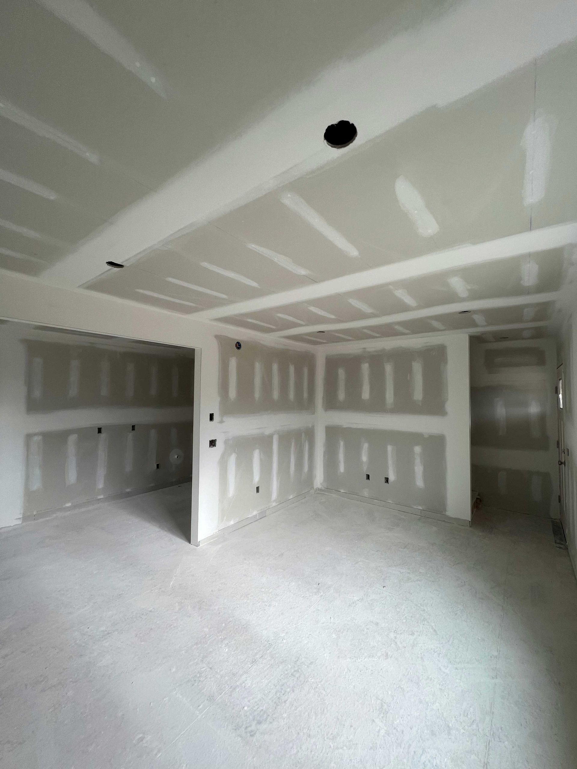 Interior of a room under construction, with drywall on walls and ceiling. Bare concrete floor.