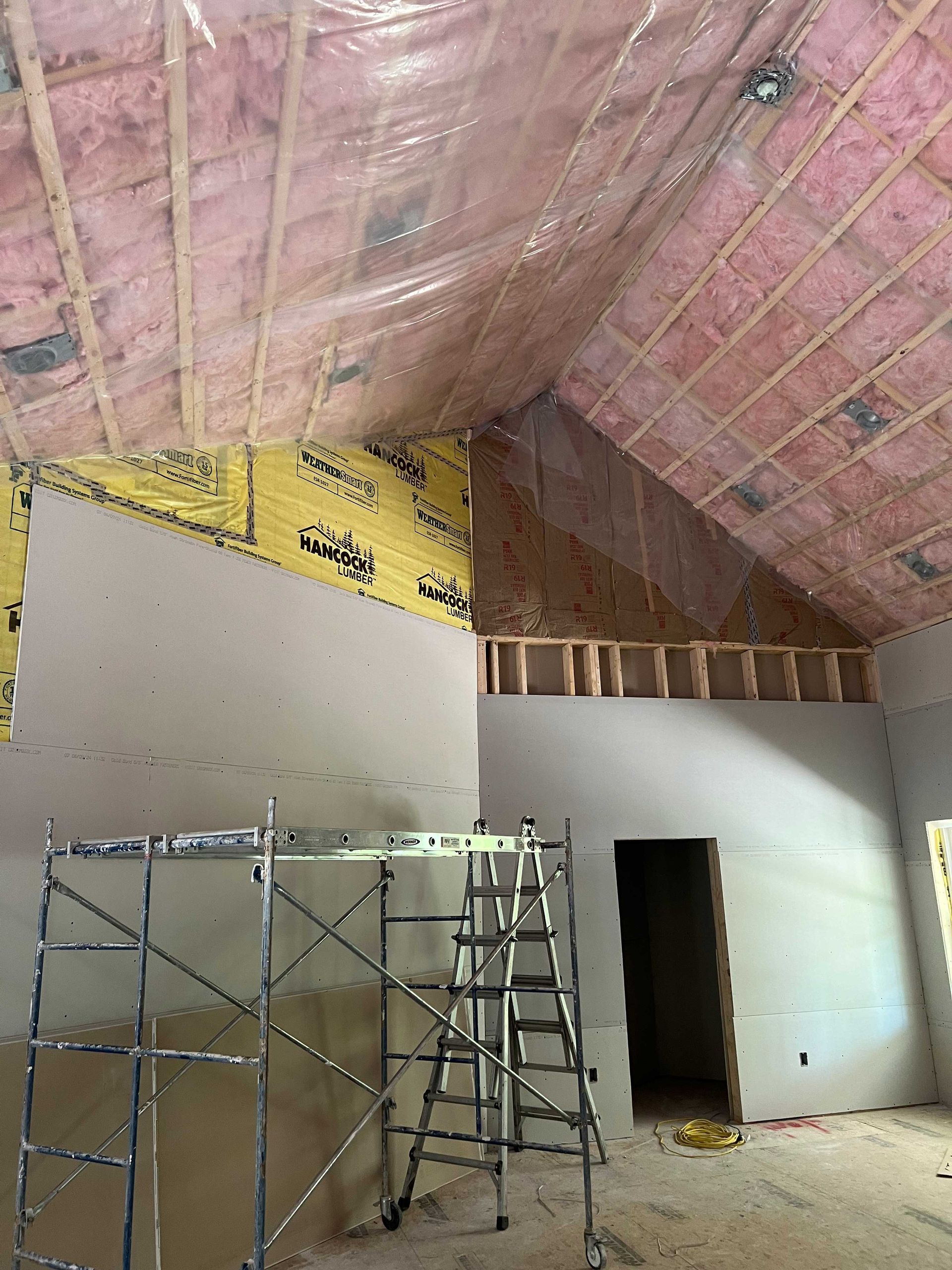 Interior view of a building under construction, showing drywall, insulation, and scaffolding.