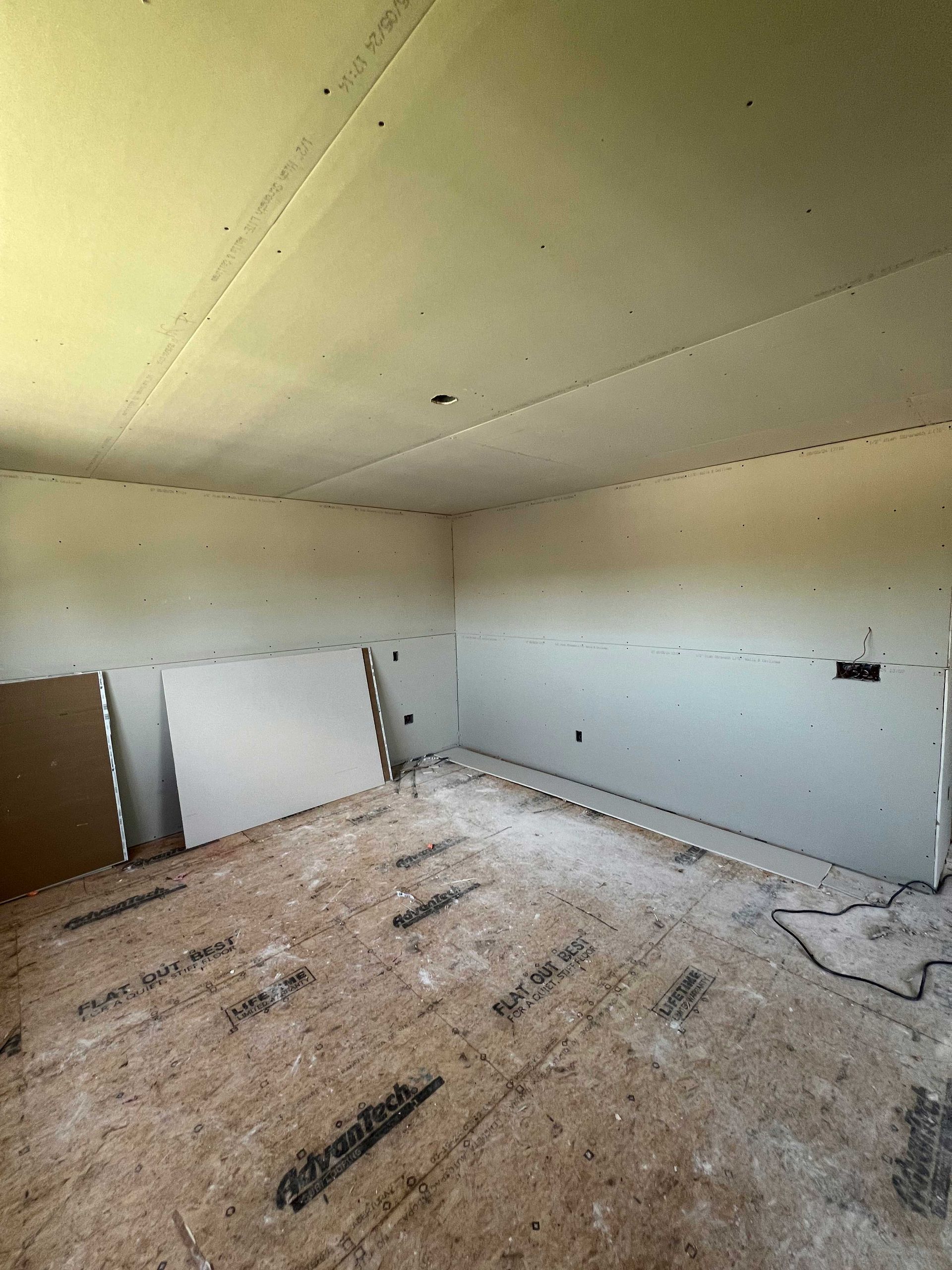 Room under construction with drywall installed on walls and ceiling; exposed wooden floor.