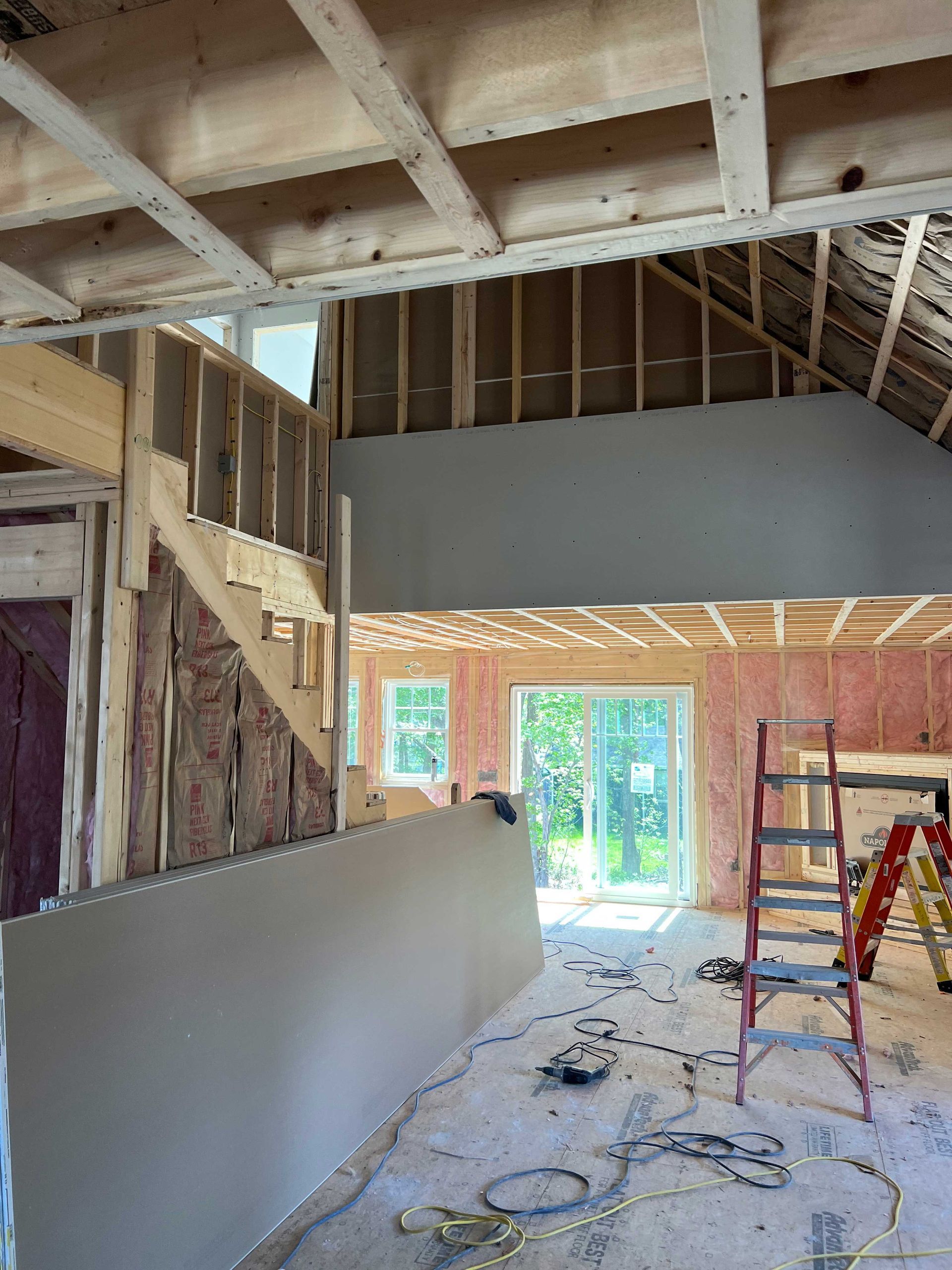 Interior view of a house under construction with exposed framing, drywall, and a staircase.