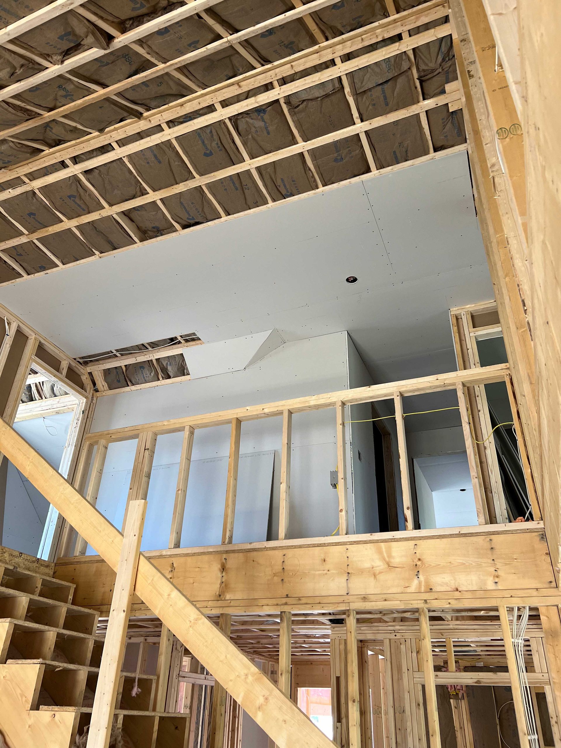 Interior of a building under construction, showing wooden framework, staircase, and unfinished ceiling with drywall.