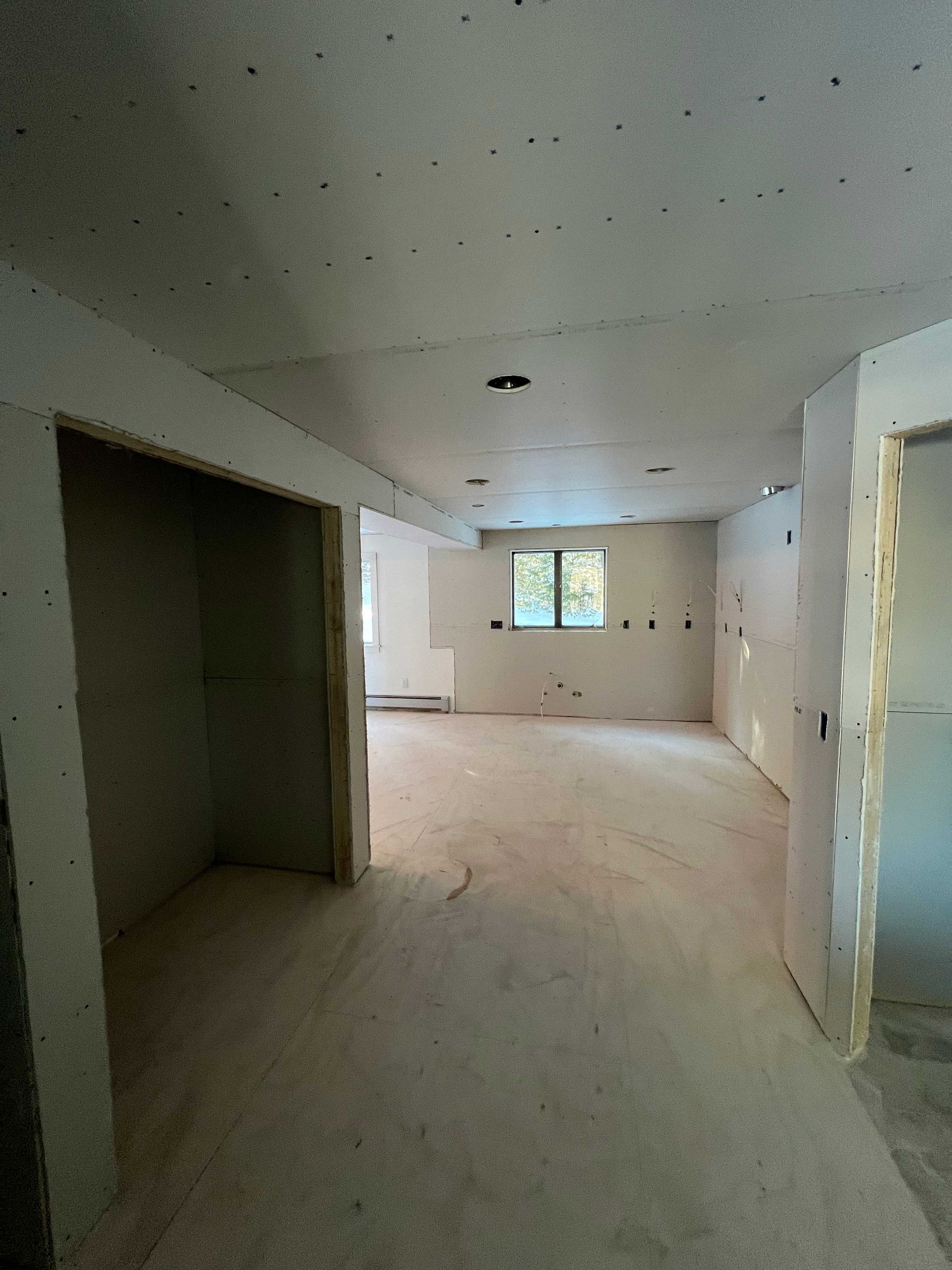 Interior of unfinished room; drywall installed on walls and ceiling; doorway frames visible.