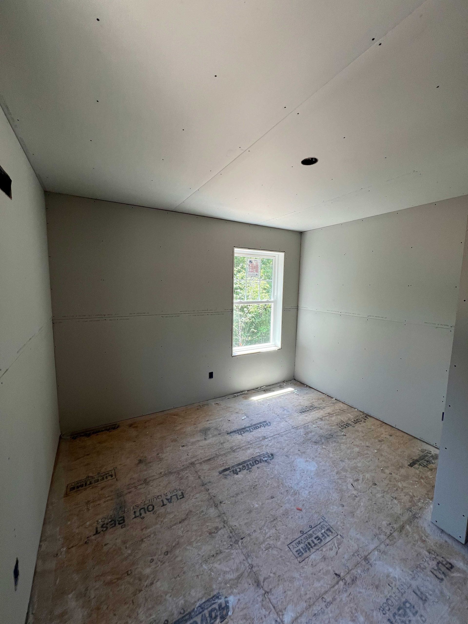 Unfinished room interior with drywall walls, window, and wood subfloor.