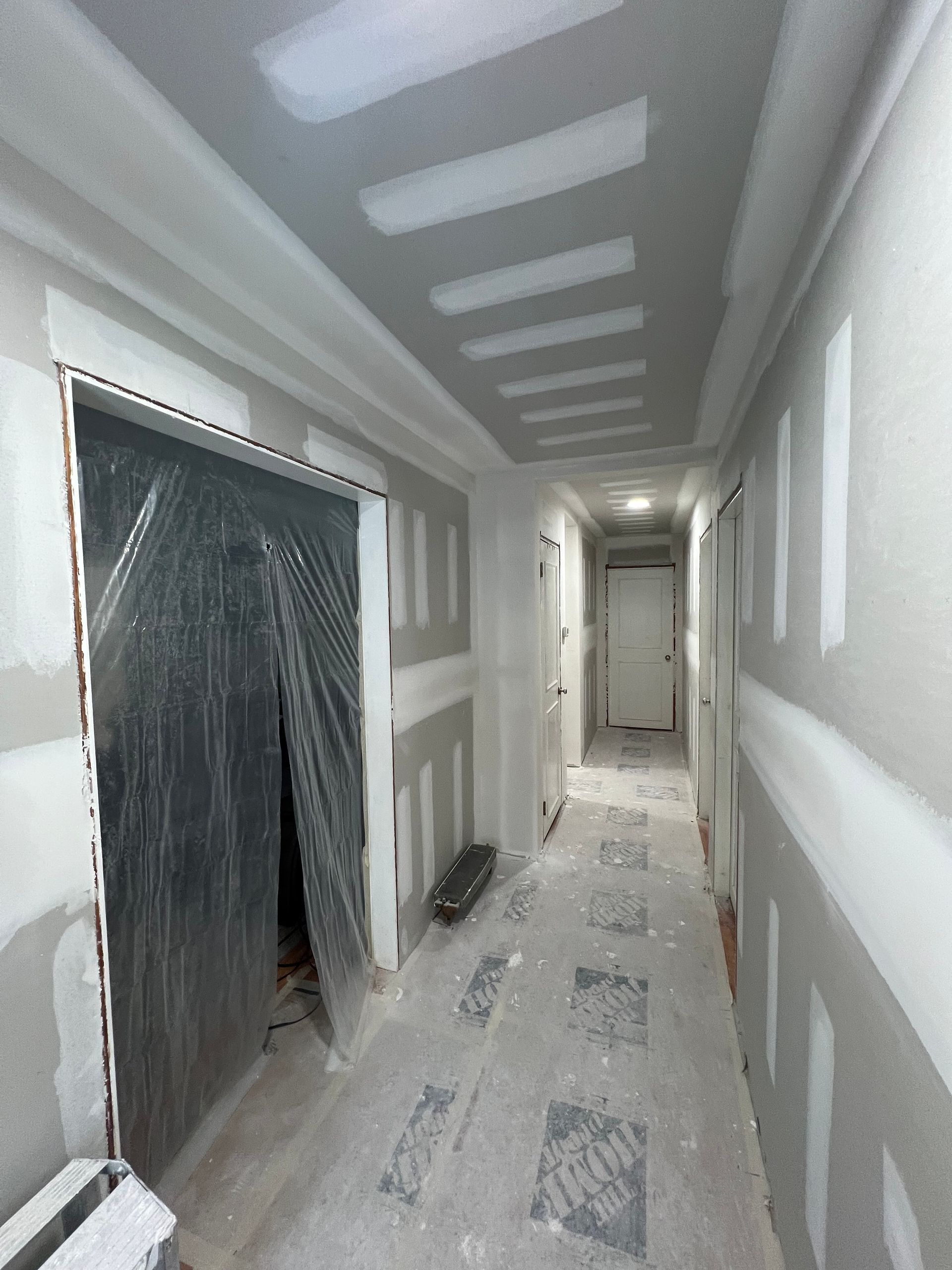 Hallway under construction with drywall and plastic sheeting.