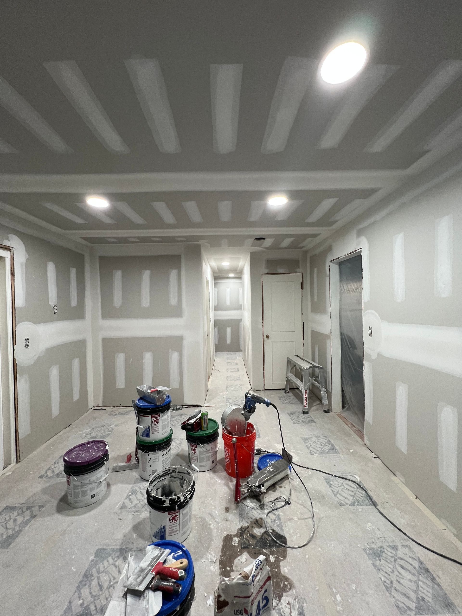 Interior under construction, drywall installed on walls and ceiling. Paint cans, tools on floor.