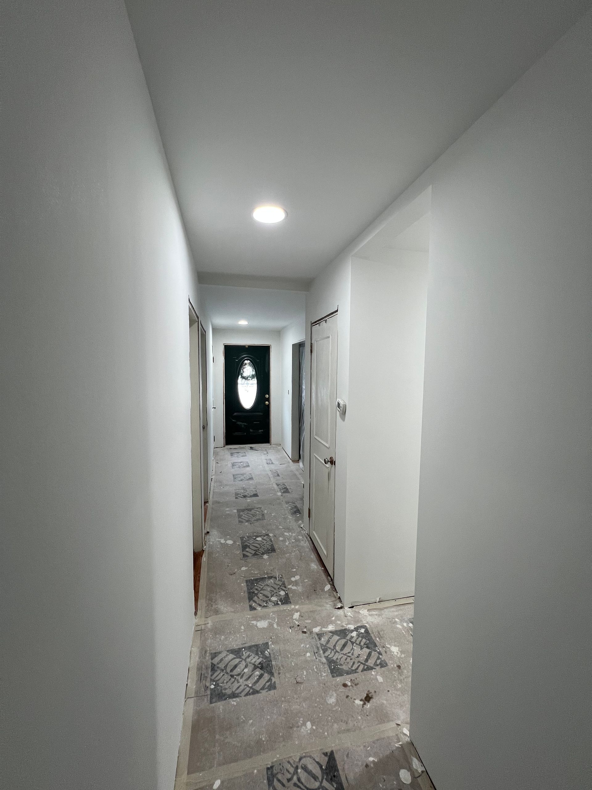 Narrow hallway with newly painted white walls, doors, and a patterned floor. A black front door is visible.