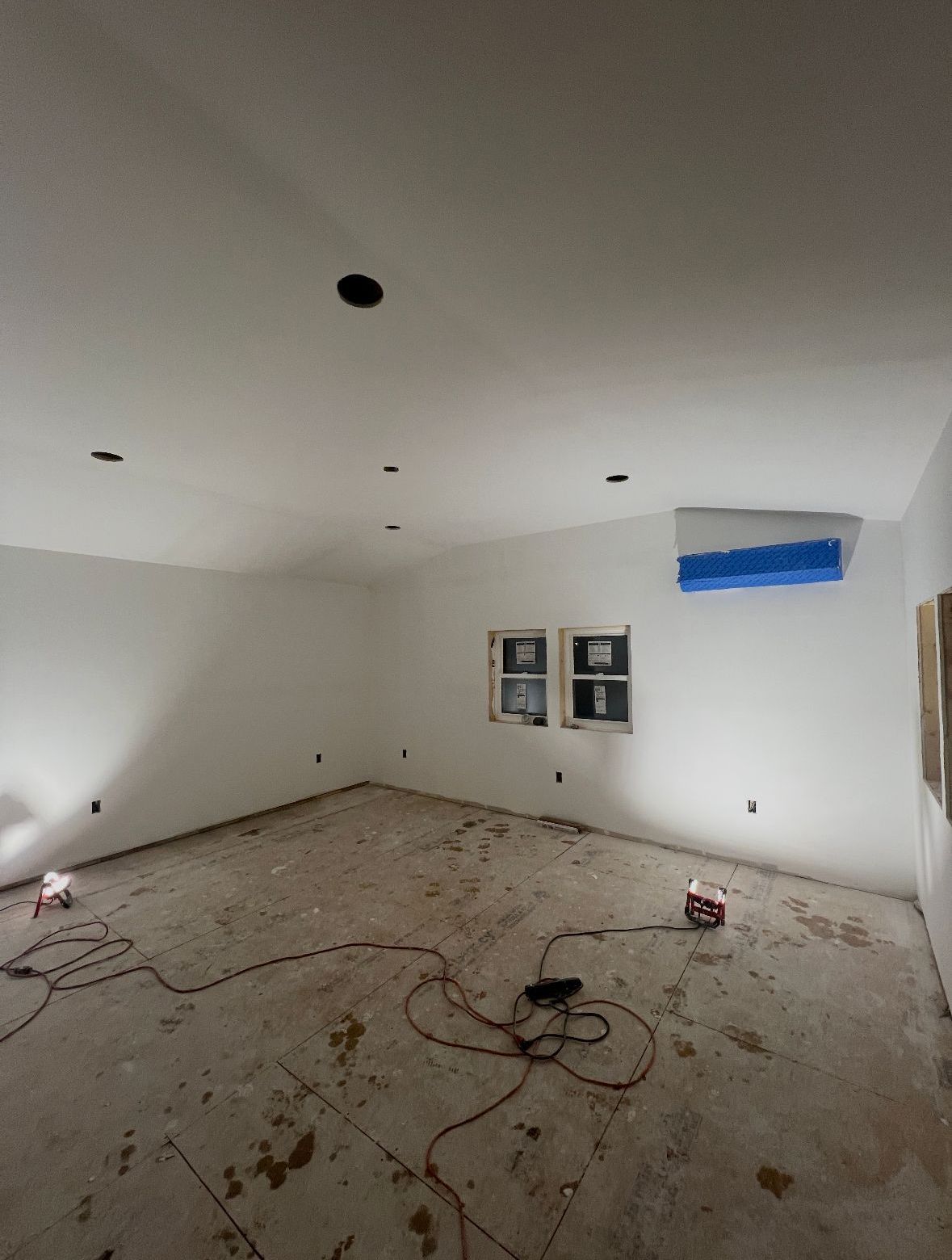 Empty room with white walls, exposed floor, recessed lighting, and two small windows.
