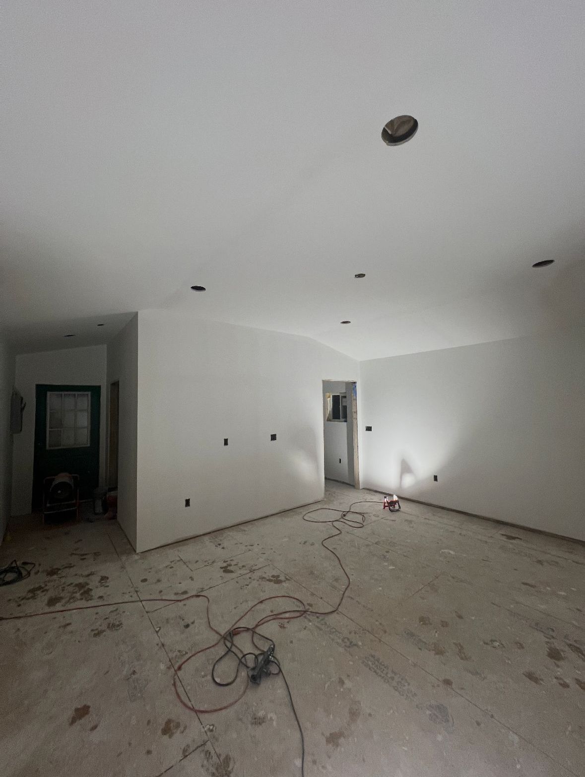 Empty room under construction with white walls, exposed wiring, and holes in ceiling. Concrete floor.