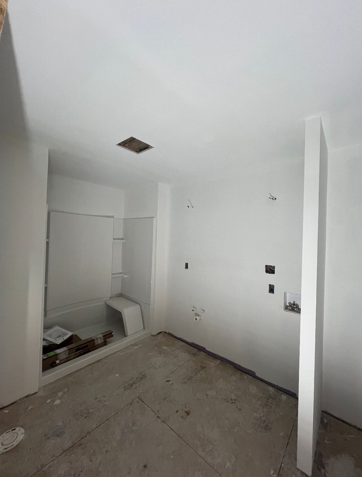 Empty bathroom under construction, white walls, shower stall, open ceiling panel, concrete floor.