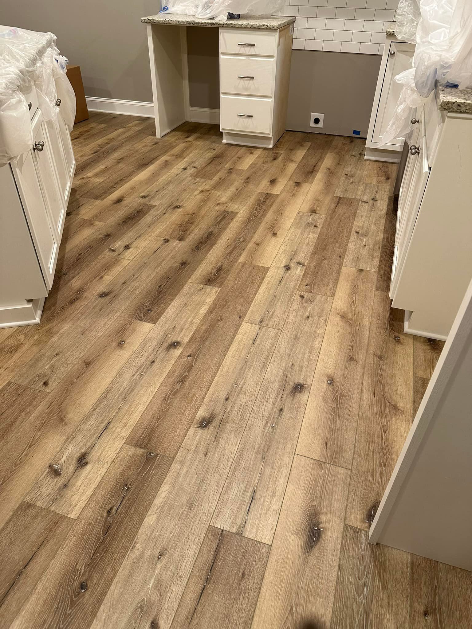 Newly installed wood-look laminate flooring in a kitchen. Cabinets and a desk are visible.