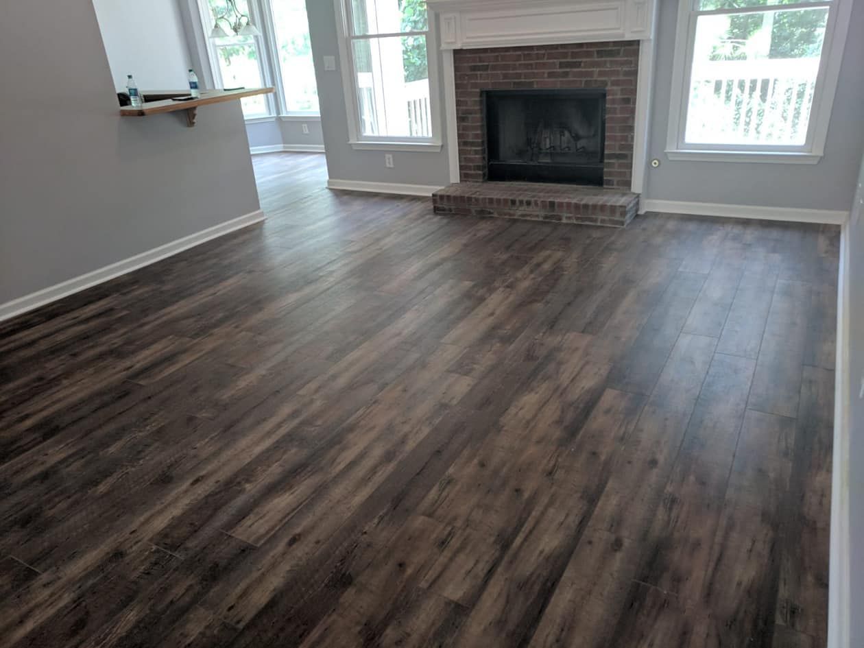 Dark wood-look flooring in a living room with a brick fireplace and windows.