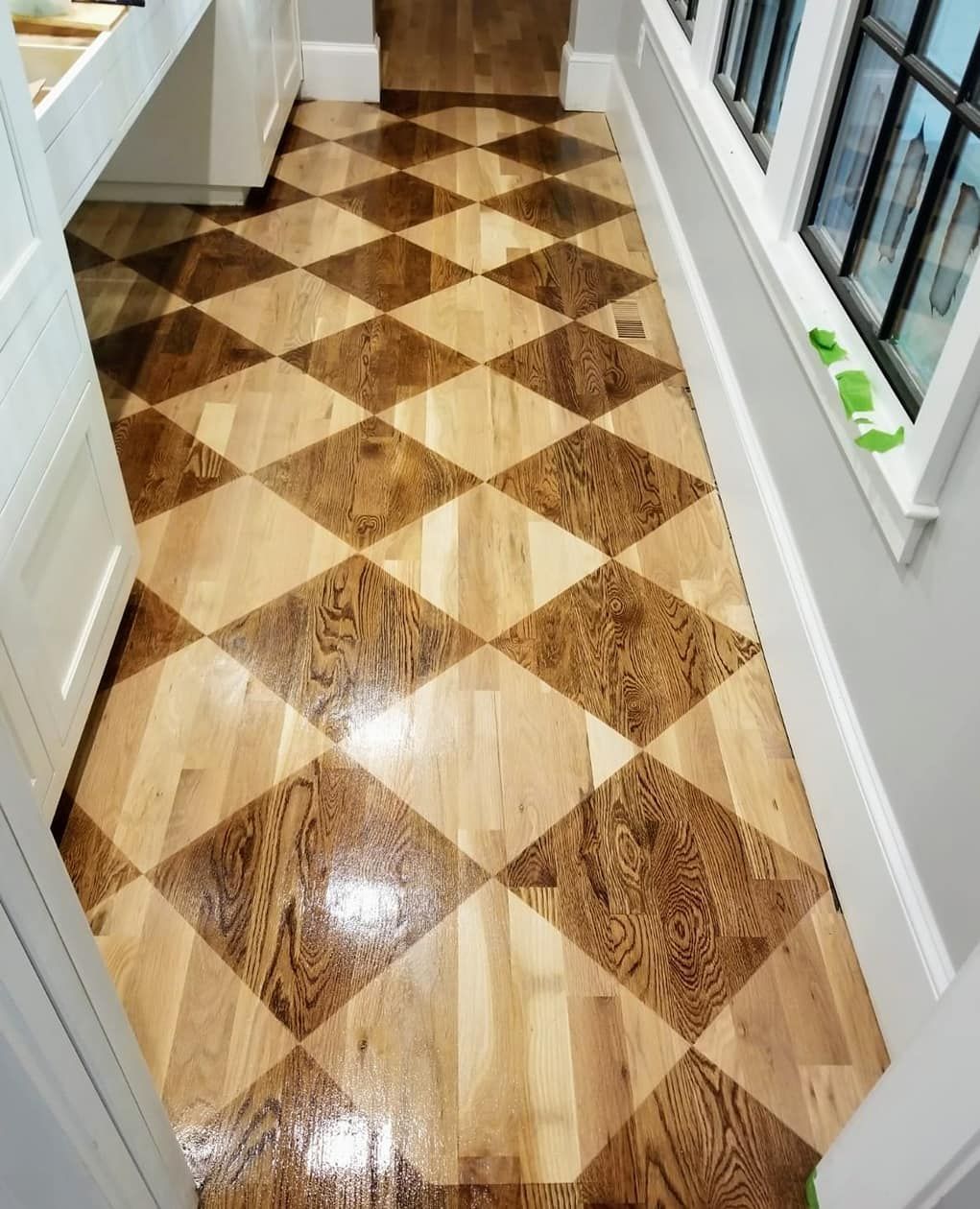 Checkerboard pattern hardwood floor in hallway with a window.