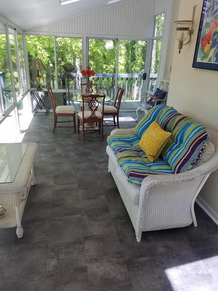Sunroom with wicker furniture, dining table, and large windows overlooking trees.