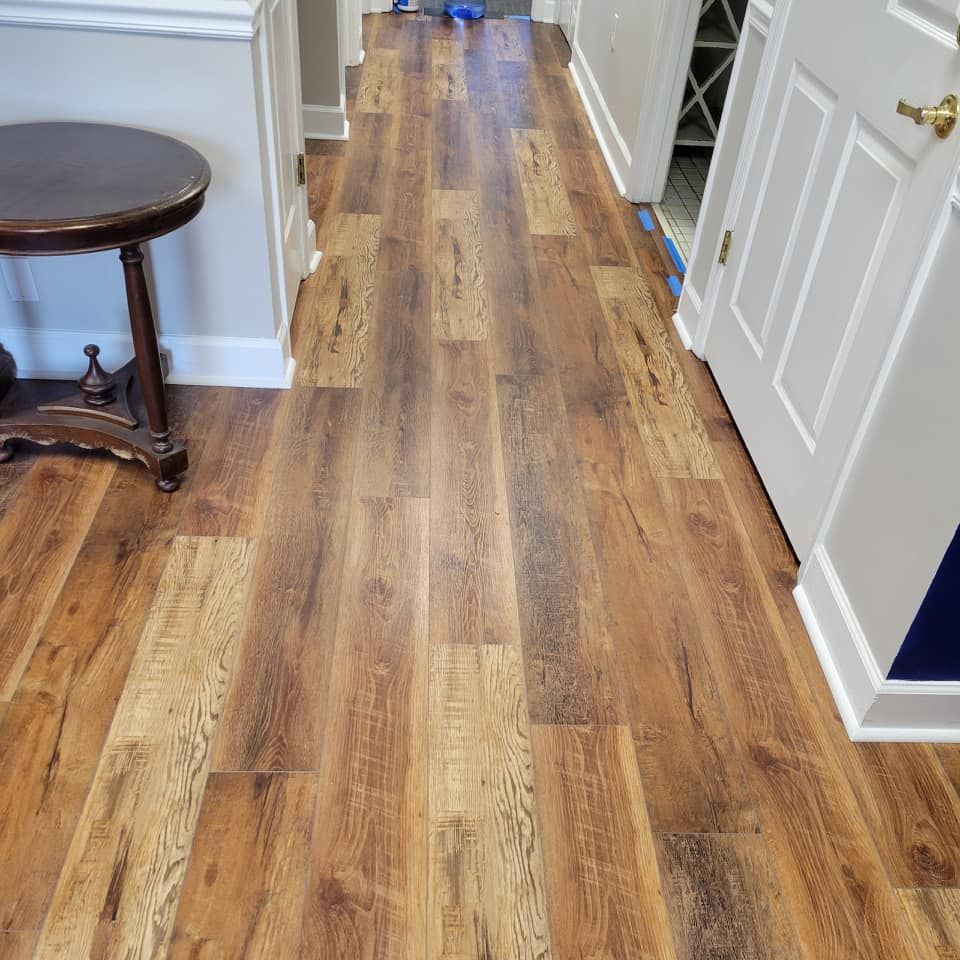 Wooden plank flooring in a hallway with a small, round table on the left and a door on the right.