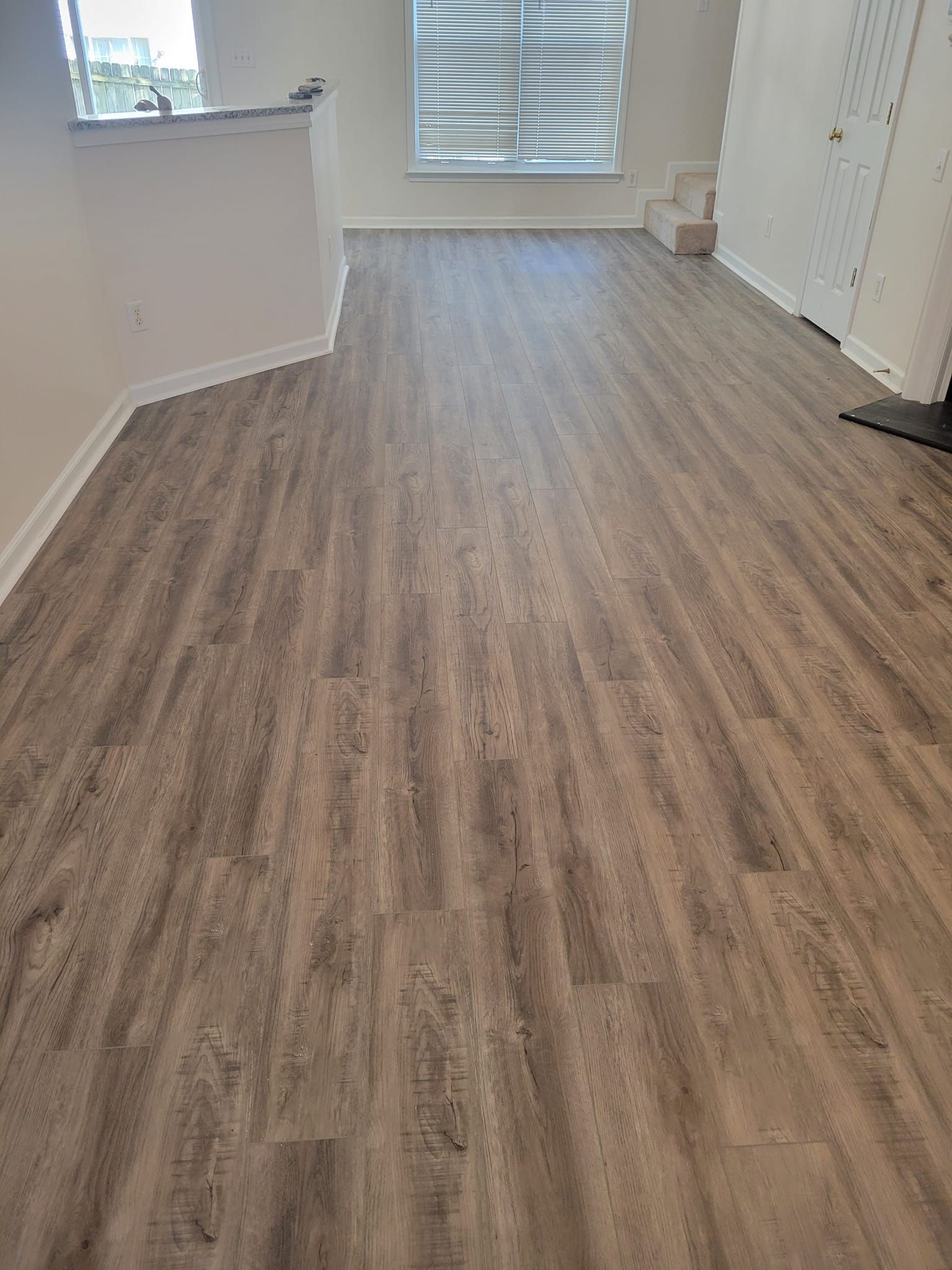Gray wood-look flooring in a room with a white wall and window with blinds.