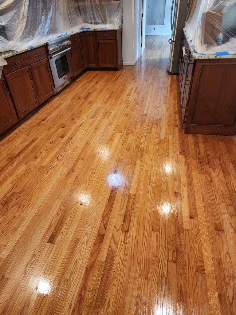 Newly refinished hardwood floor in a kitchen, reflecting light. Brown cabinets line the walls.